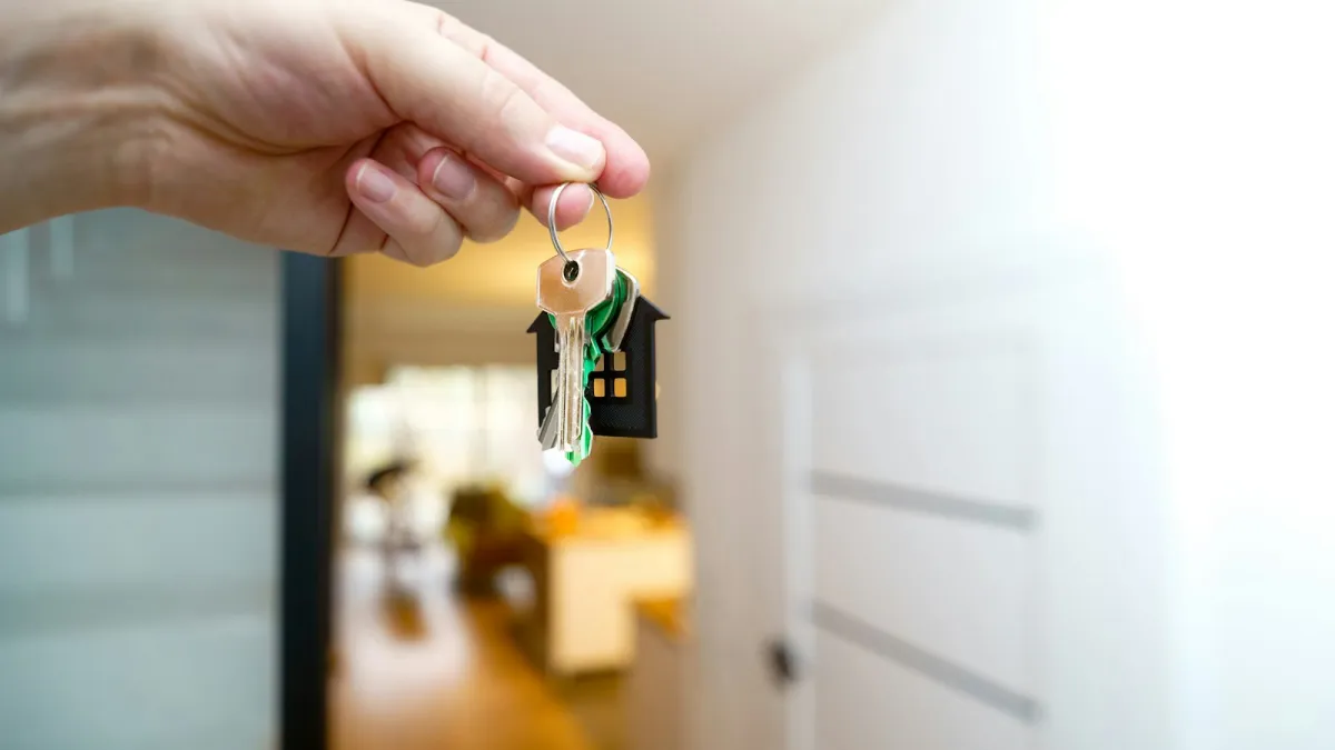A hand holds house keys on a house-shaped key ring