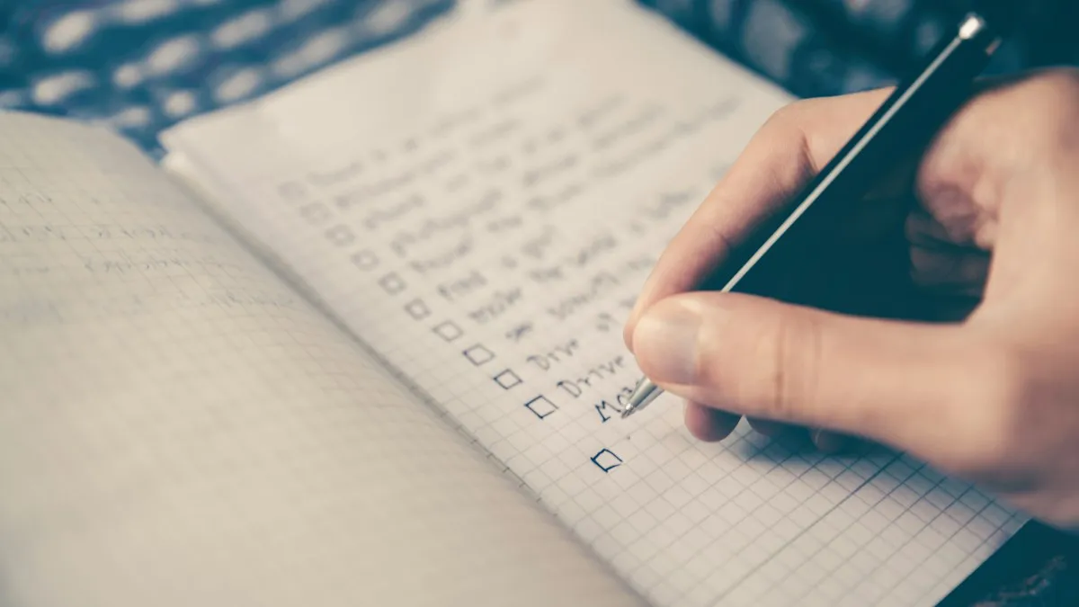 Une main écrit une liste à cocher dans un carnet